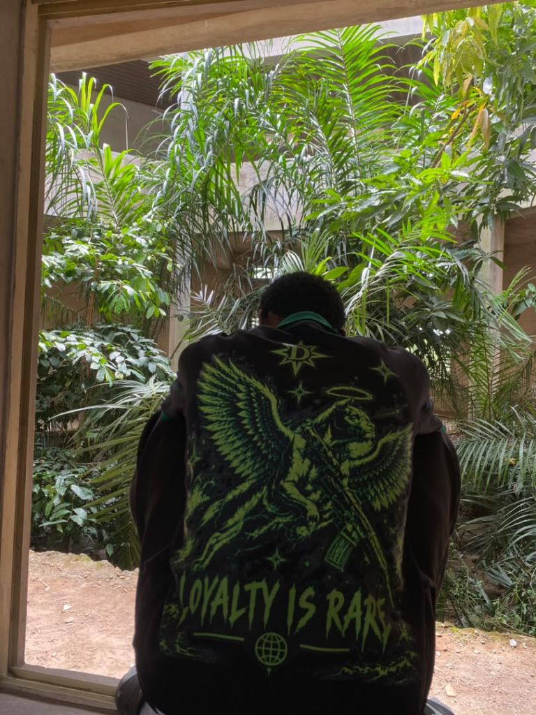 Model wearing the Loyalty Is Rare Seraph jersey in black and venom green, back view facing a garden
